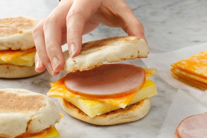 A person putting a muffin on a cheese and bacon sandwich